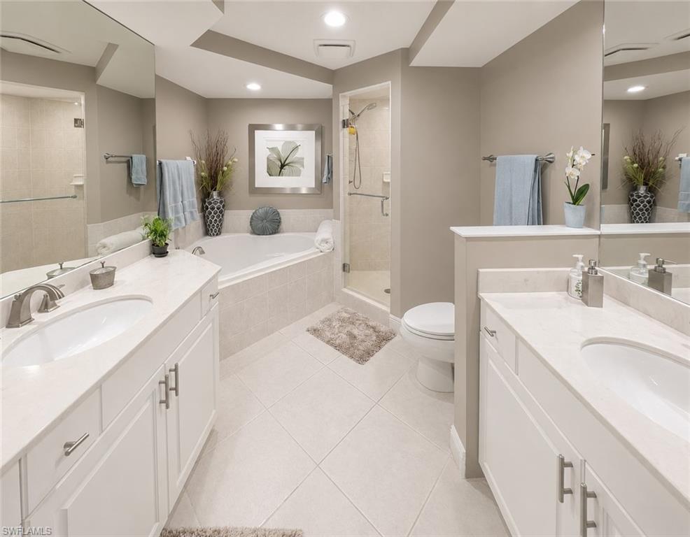 Bathroom featuring a large soaking tub, glass-enclosed shower, dual vanities with integrated sinks, and tiled flooring