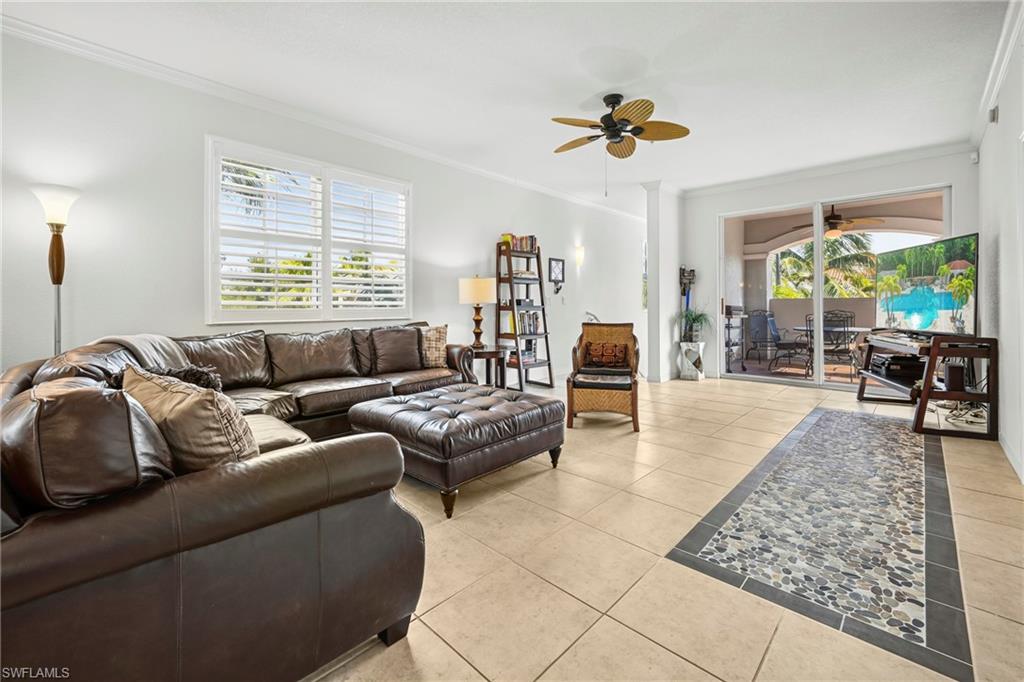 Light-filled living area featuring neutral tile flooring with a decorative pebble inlay, crown molding, and a ceiling fan