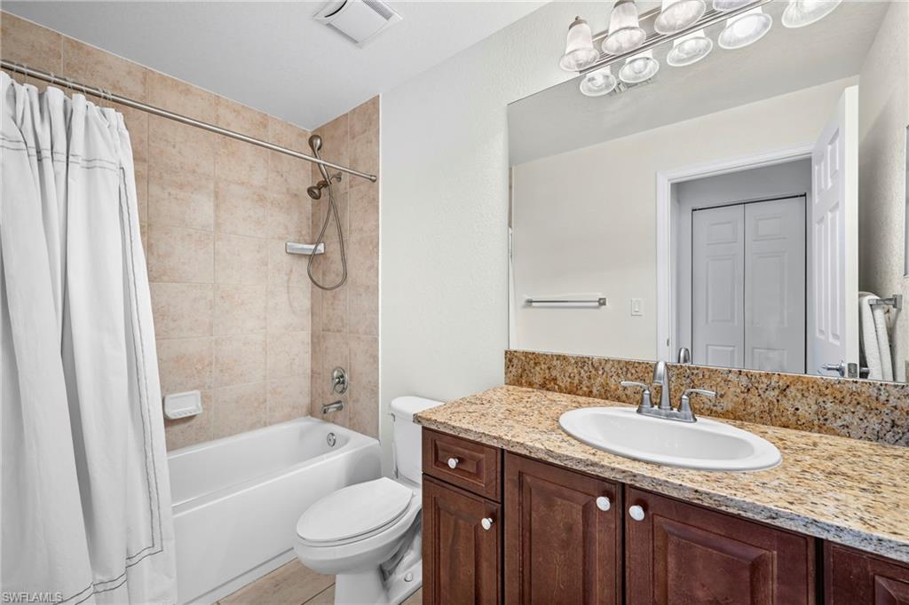 Full bathroom featuring a rich wood-finish vanity with a granite countertop and an undermount sink