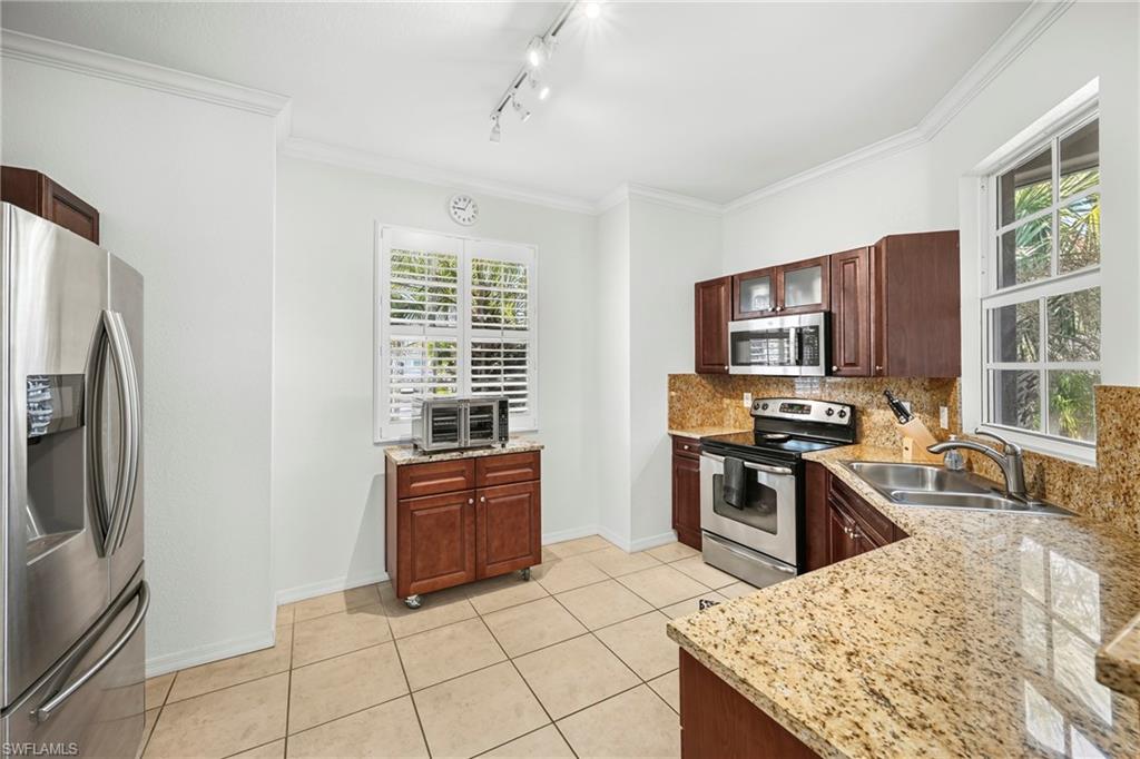 Kitchen featuring granite countertops, stainless steel appliances, dark wood cabinetry, tile flooring, and track lighting