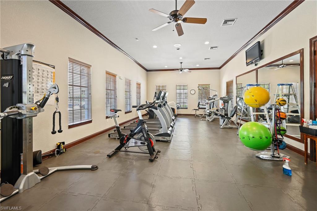 Spacious fitness center featuring neutral walls, dark trim, multiple windows with blinds, ceiling fans, and impact-absorbing flooring