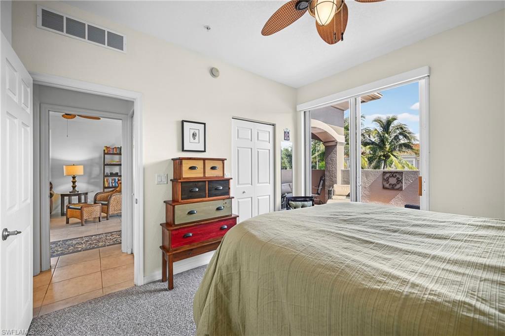 Carpeted bedroom featuring a ceiling fan with integrated lighting, sliding glass doors opening to a private patio, and a separate doorway leading to a tiled interior space