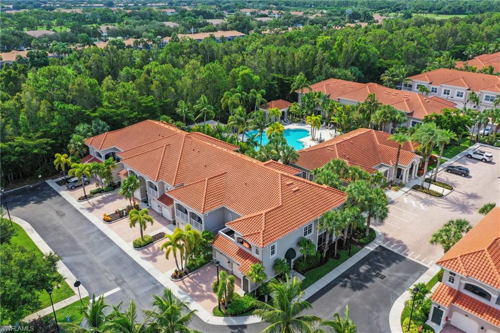 Residential complex featuring multiple buildings with terracotta-style tile roofs, a central swimming pool with surrounding lounge areas, and paved parking facilities