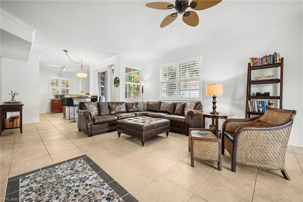 Spacious living area featuring large format tile flooring, crown molding, and plantation shutters