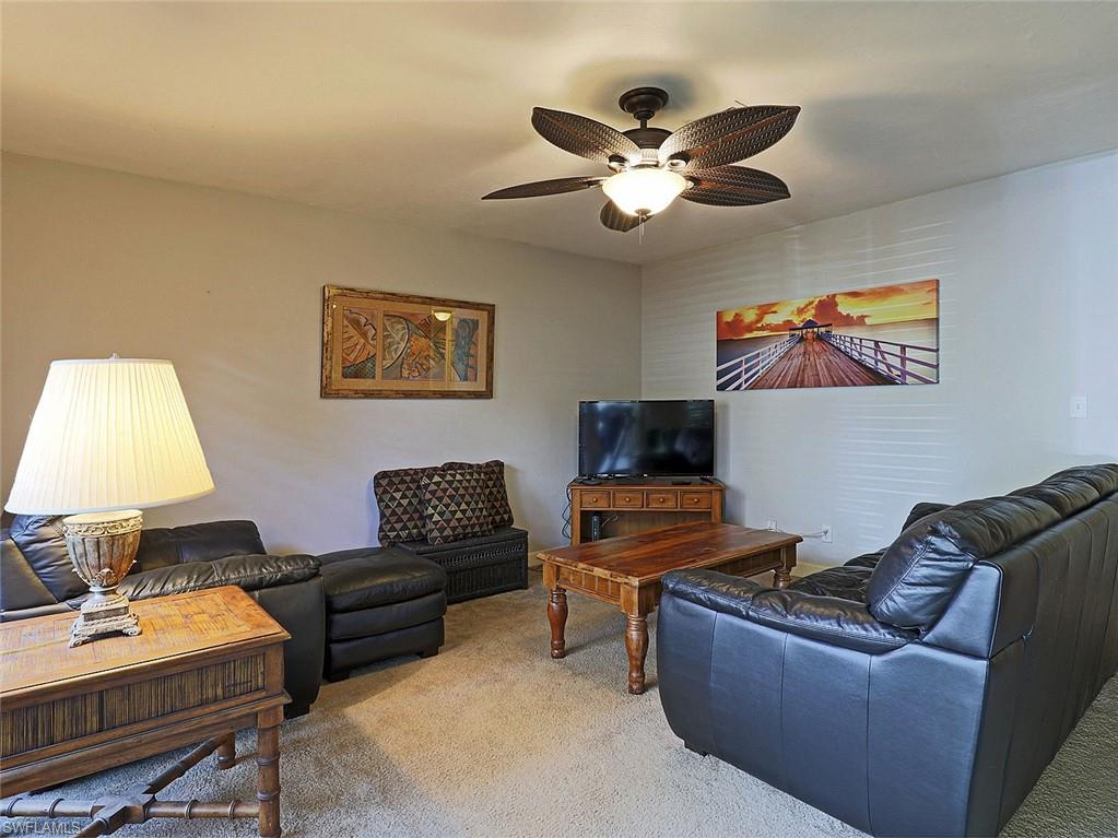 Carpeted living space featuring a ceiling fan with light fixture, light gray wall tones, and built-in wall texture