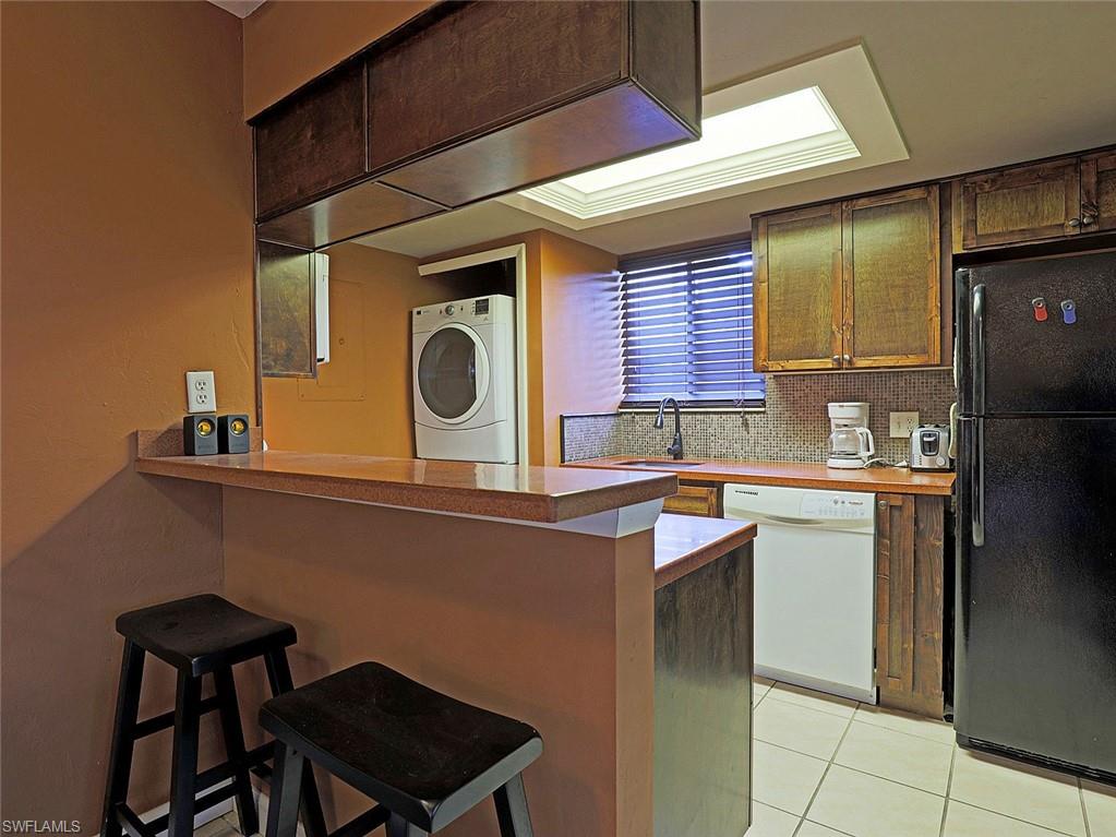 Kitchen featuring a breakfast bar with stone-finish countertop, wood-finish cabinetry, tile backsplash, and tile flooring