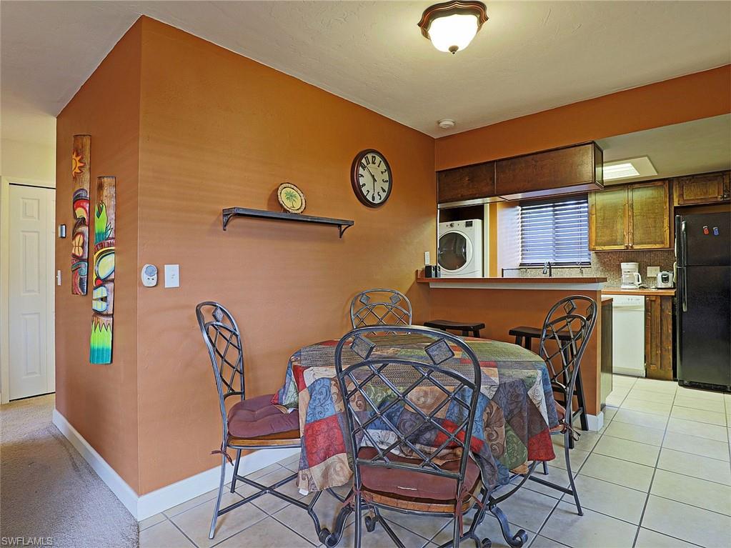 Kitchen and dining area featuring a breakfast bar, white tile flooring, wood-finish cabinetry, and a stacked washer and dryer