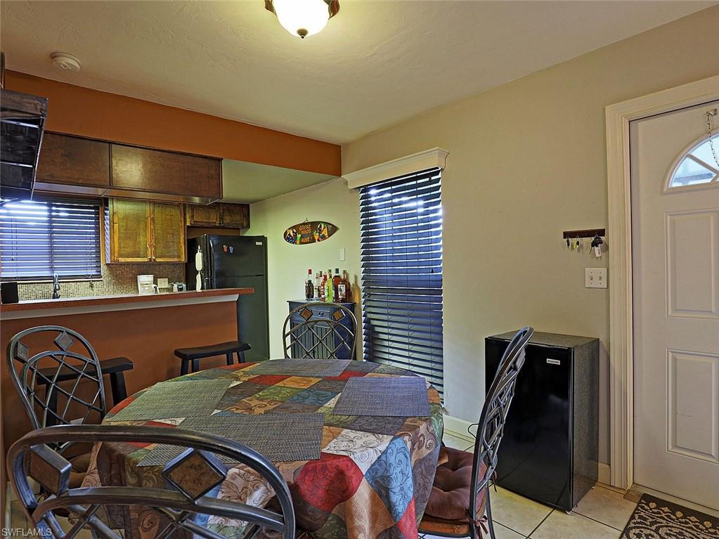 Compact kitchen and dining area featuring a breakfast bar, wood-finish cabinetry, tile flooring, a window with horizontal blinds, and a white paneled entry door