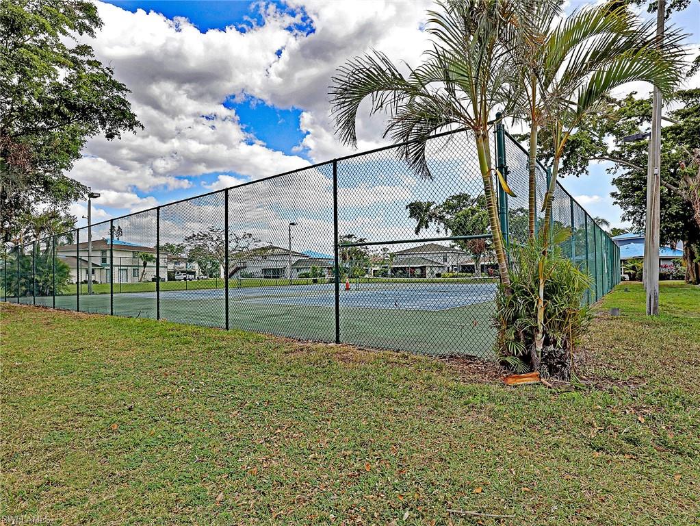 Fenced tennis court featuring a blue playing surface and green surrounding area