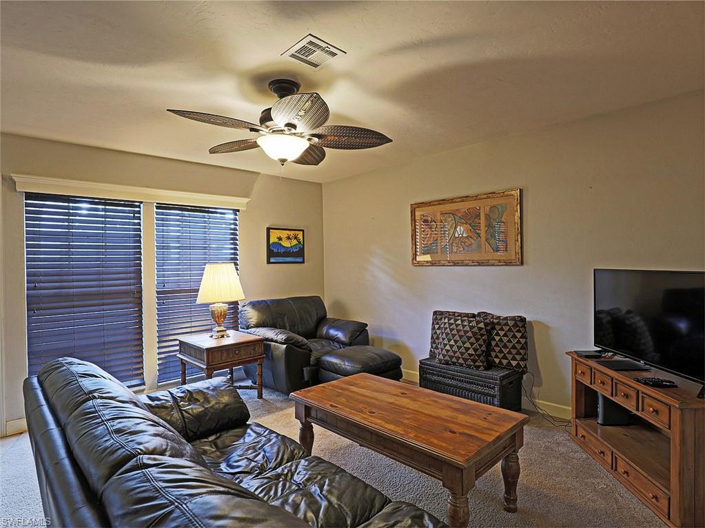 Living area with a ceiling fan, dual windows featuring horizontal blinds, and carpeted flooring