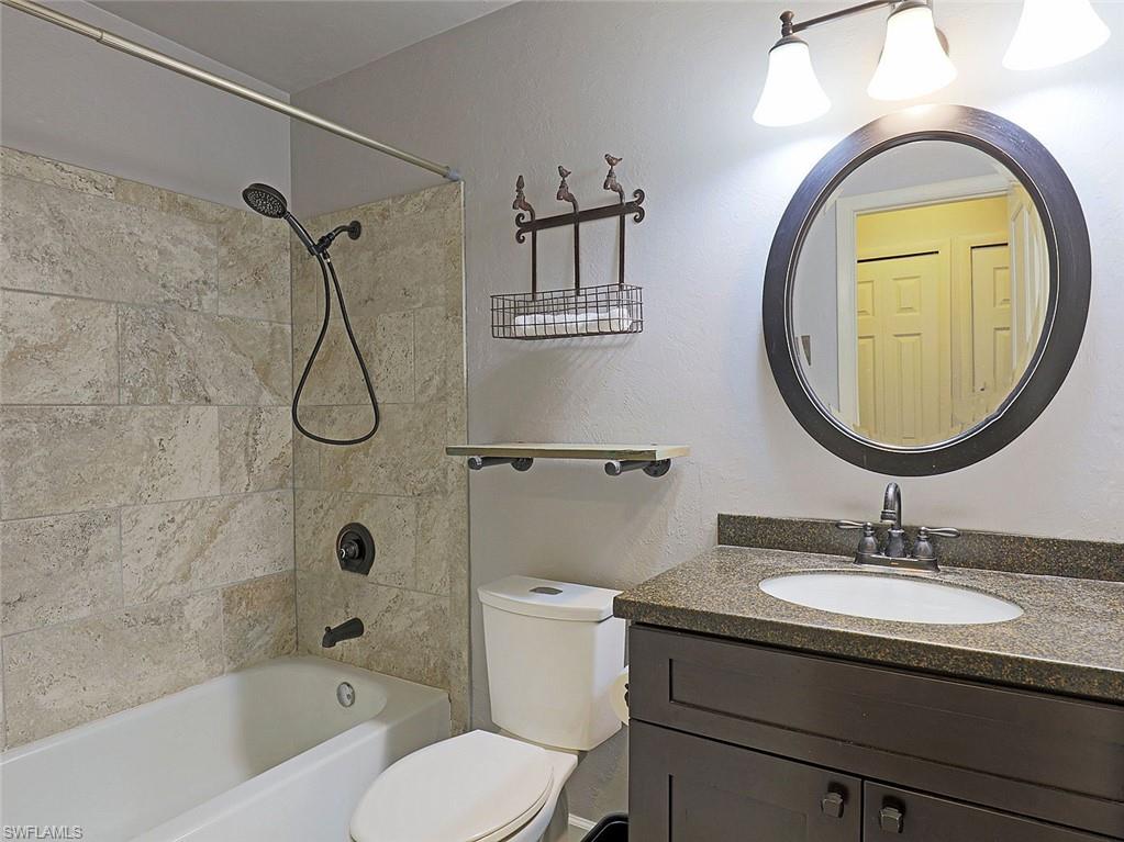 Bathroom featuring a dark wood-finish vanity with a stone-look countertop, an oval undermount sink, and a circular framed mirror