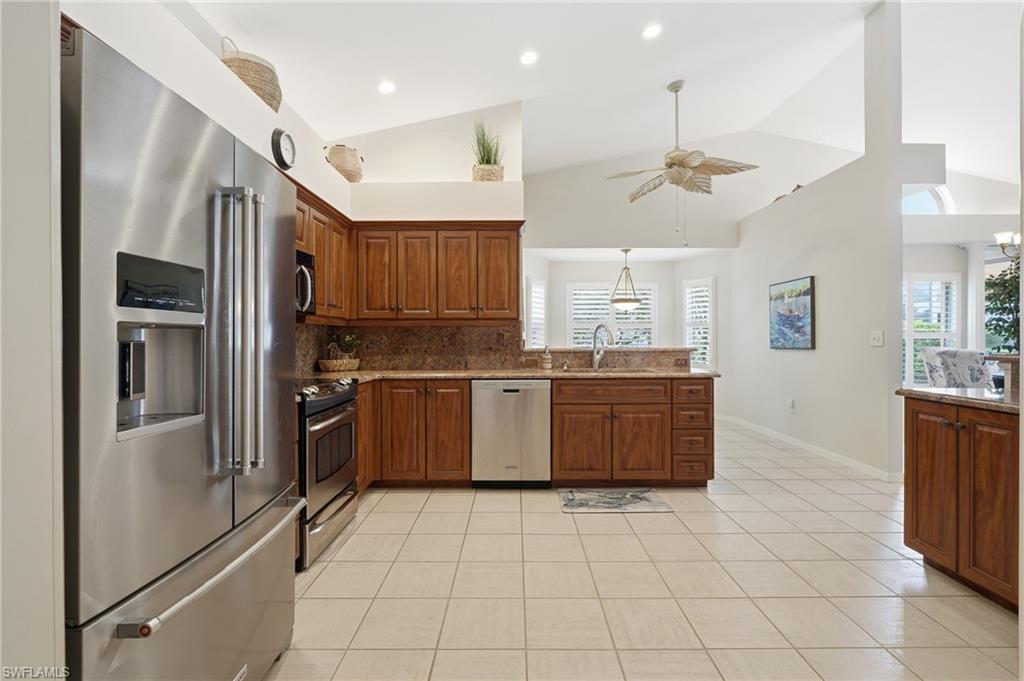 Kitchen featuring stainless steel appliances, wood-finish cabinetry, stone countertops, and tile flooring