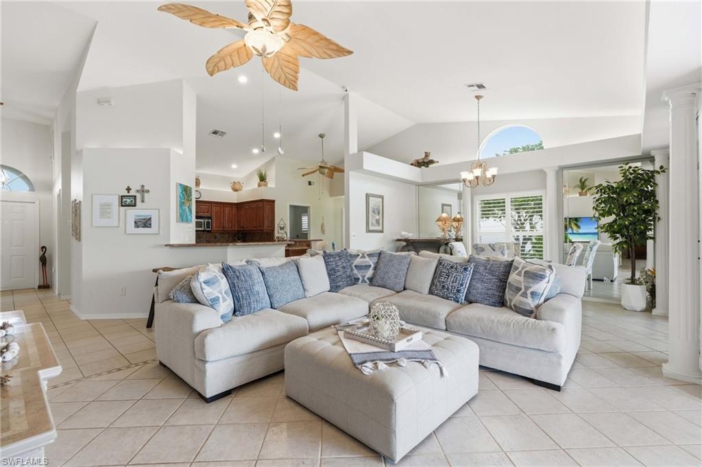 Vaulted ceilings featuring a palm-leaf style ceiling fan, tile flooring throughout, and a half-wall kitchen bar with a granite countertop