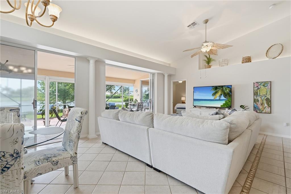 Spacious living area featuring large sliding glass doors, coffered ceilings, column accents, and neutral tile flooring with a decorative inlay