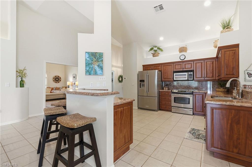 Kitchen featuring stainless steel appliances, wood-finish cabinetry, granite countertops, and tile flooring