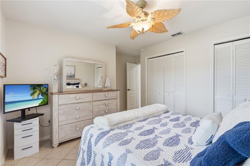 Room featuring tile flooring, a ceiling fan with leaf-shaped blades, and two sets of louvered bi-fold closet doors