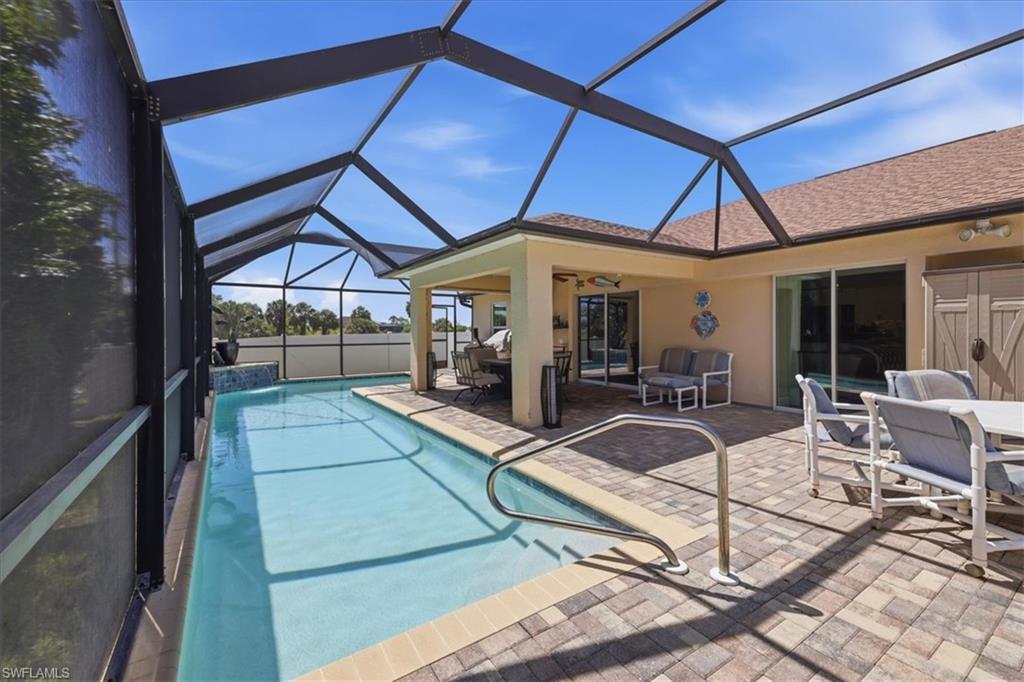 Screened-in pool enclosure featuring a rectangular pool with handrail, a covered patio area, and an expansive paver deck