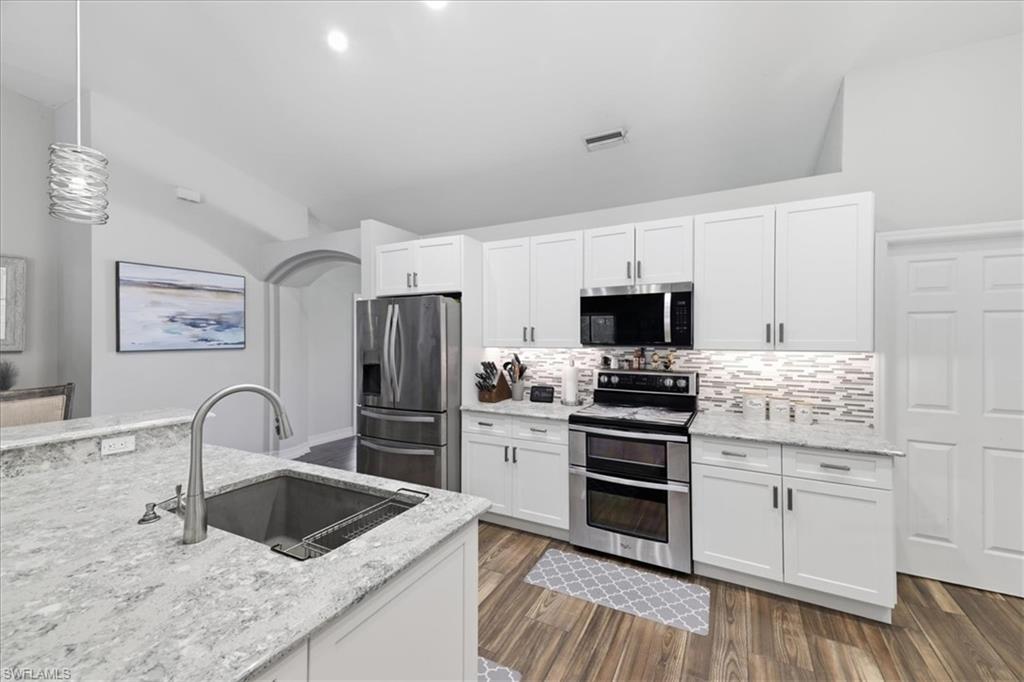 Modern kitchen featuring white shaker cabinetry, stainless steel appliances, speckled countertops, and wood-finish flooring