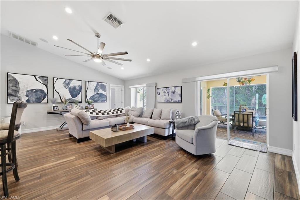 Spacious living area featuring vaulted ceilings, wood-finish flooring, recessed lighting, a large ceiling fan, and sliding glass doors leading to a screened lanai with a tiled floor