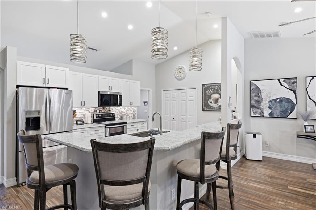 Kitchen featuring an island with stone countertops, stainless steel appliances, white cabinetry with dark hardware, a mosaic tile backsplash, and wood-finish flooring