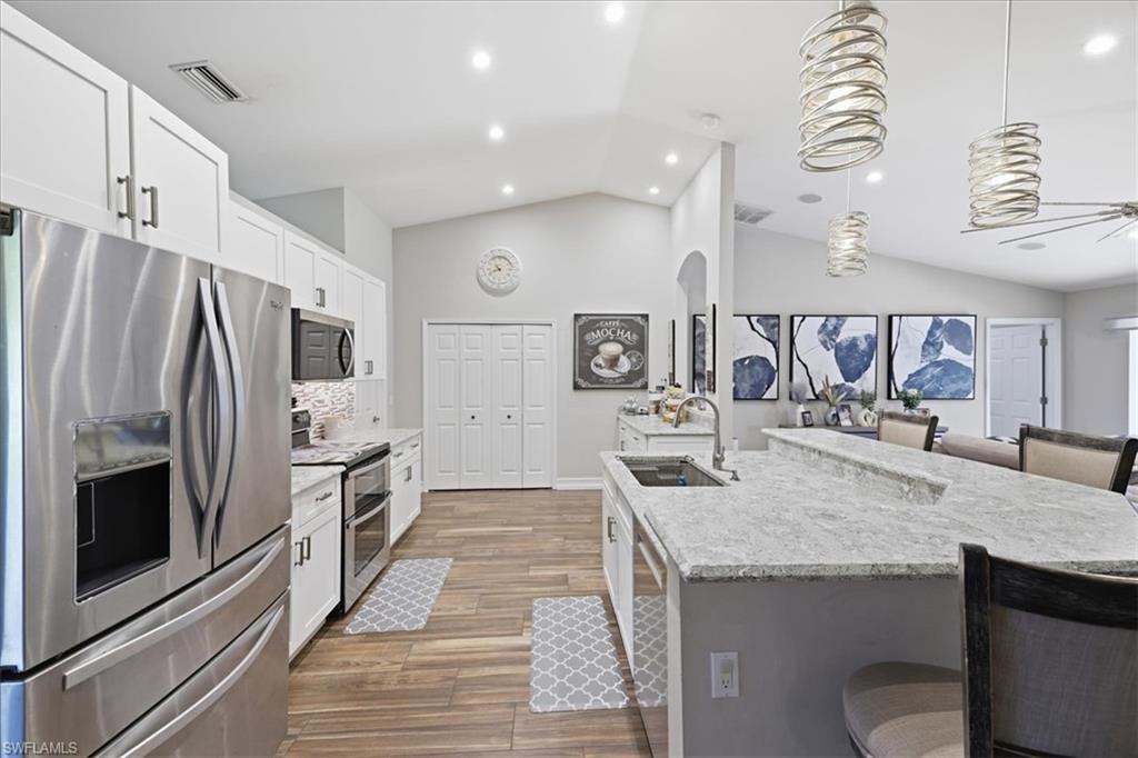Spacious kitchen featuring white cabinetry, stainless steel appliances, light-toned countertops, wood-finish flooring, and recessed lighting