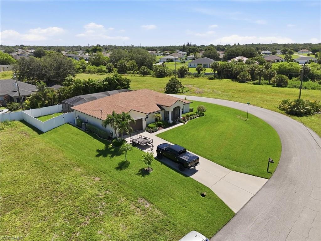 Exterior featuring a terracotta tile roof, screened enclosure, concrete driveway, and mature landscaping