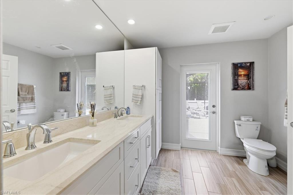 Bright bathroom featuring a dual vanity with light-toned countertops, white cabinetry, and wood-finish tile flooring