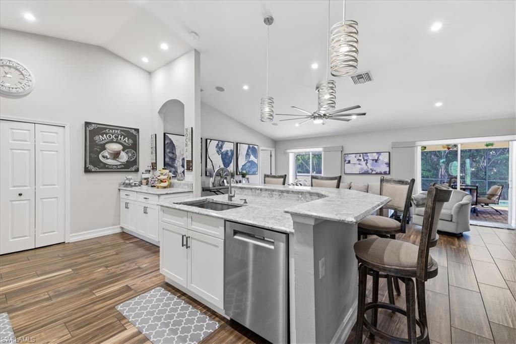 Open-concept kitchen featuring white cabinetry, stone countertops, a stainless steel dishwasher, and wood-finish flooring