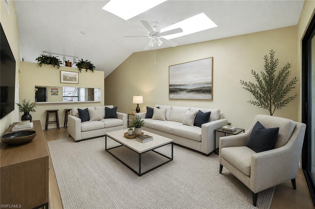 Expansive living area featuring vaulted ceilings, two skylights, a ceiling fan, and light wall tones