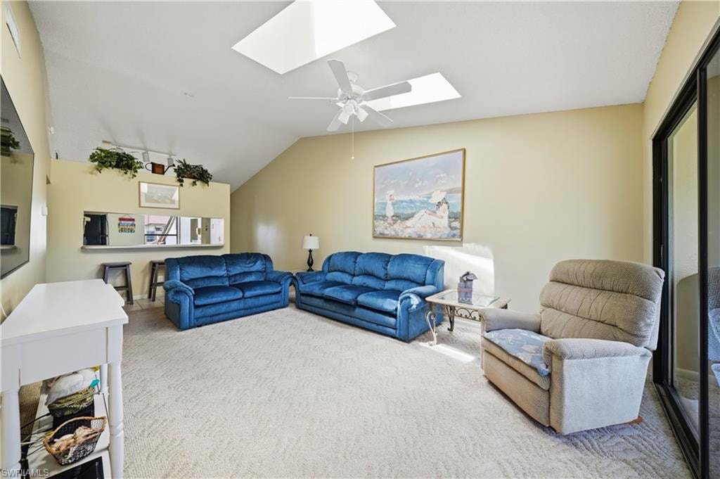 Vaulted ceilings with skylights and a ceiling fan, plush carpeting, and a built-in pass-through counter with tiled flooring