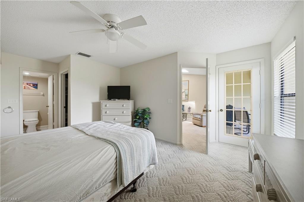 Carpeted bedroom featuring a ceiling fan, a white paneled door with glass inserts, a window with blinds, and a private attached bathroom with a toilet