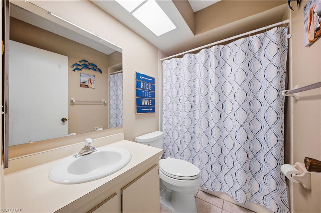 Bathroom featuring a single vanity with an integrated sink, an overhead skylight, and a bathtub with a shower curtain