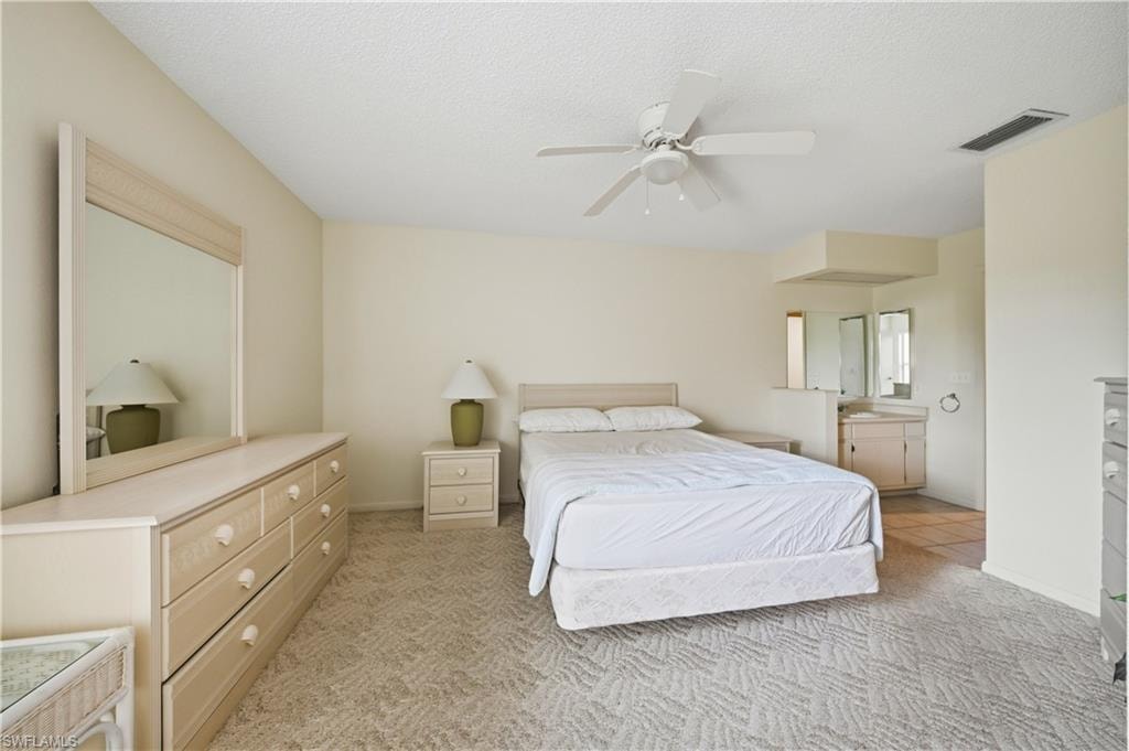 Bedroom featuring wall-to-wall patterned carpeting, a ceiling fan, and an integrated vanity area with a counter and mirrors