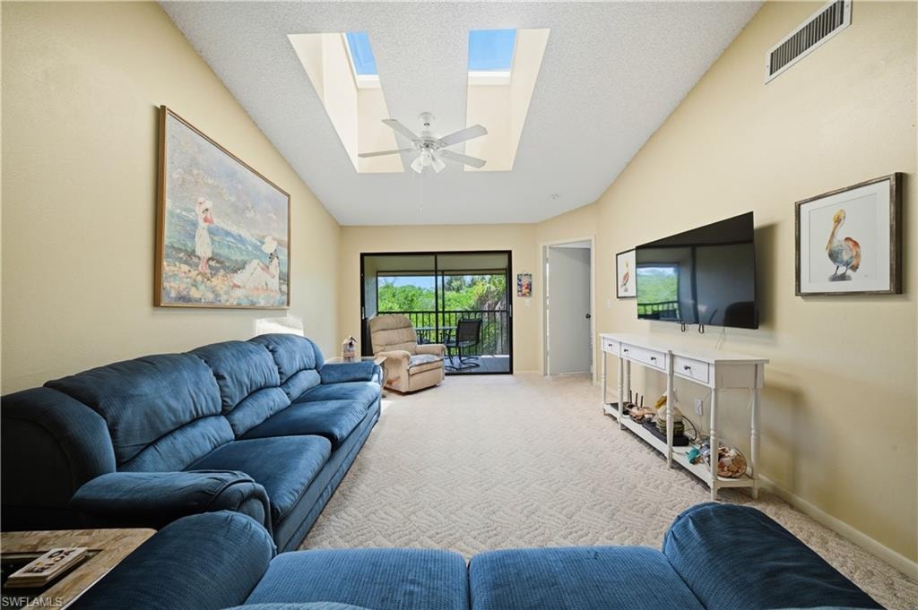 Vaulted ceiling living area featuring twin skylights, a ceiling fan, light-toned carpeting, and access to a screened balcony
