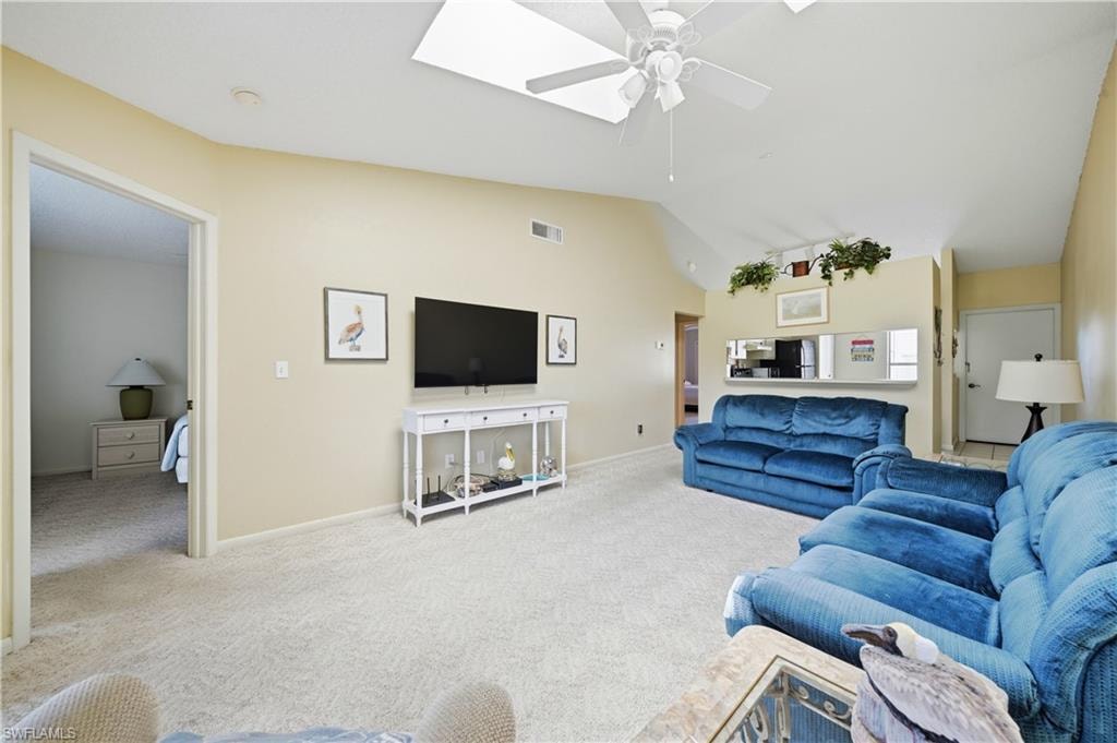 Vaulted ceiling living area featuring a ceiling fan, central skylight, light-toned carpeting, and a pass-through window with a countertop