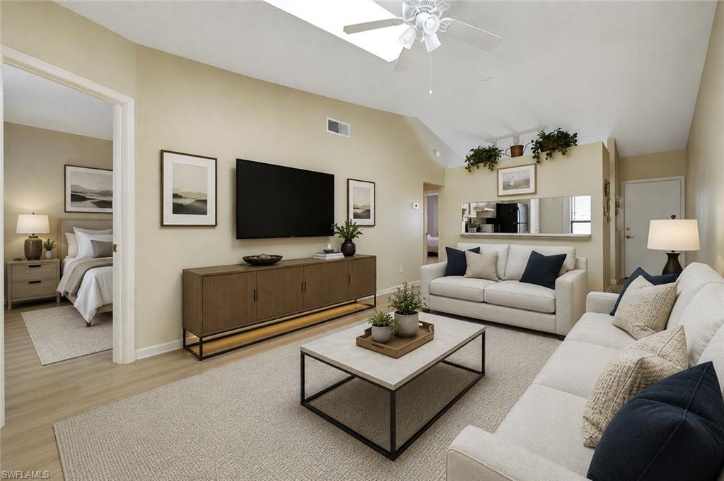 Living area featuring a vaulted ceiling with a skylight, wood-finish flooring, and a ceiling fan