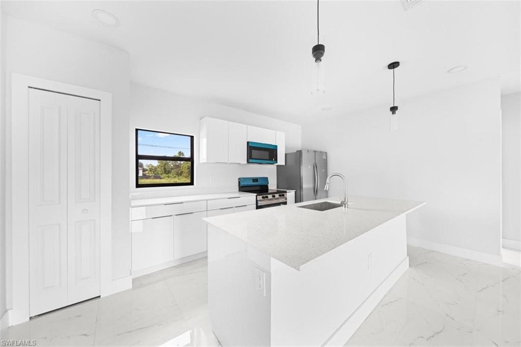 Kitchen featuring a central island with an integrated sink, white cabinetry, and stainless steel appliances