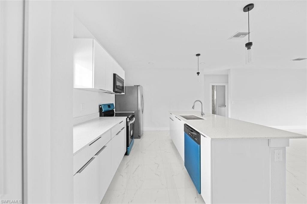 Bright kitchen showcasing an expansive island with an integrated sink and modern pendant lighting
