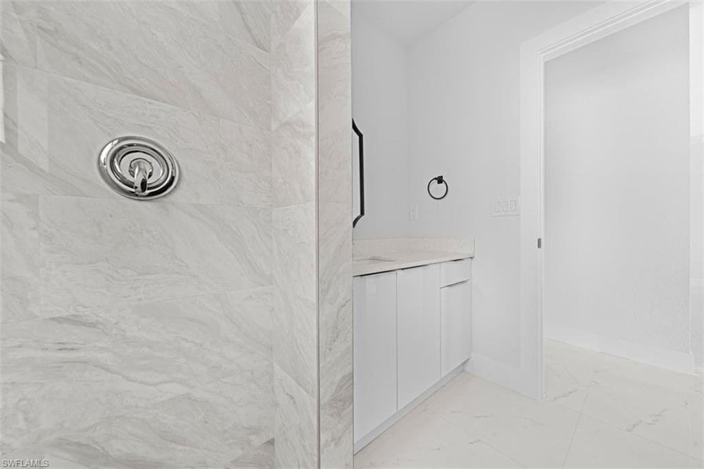 Shower featuring light-toned, veined wall tile and a polished chrome shower control