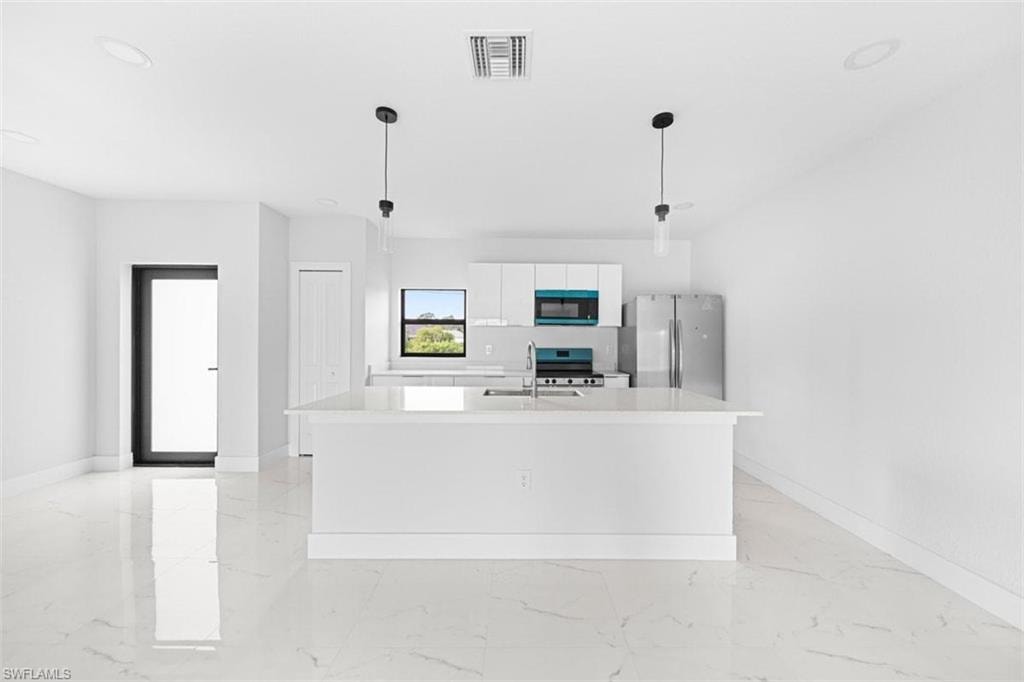 Open-concept living space featuring sleek white flooring, a kitchen island with sink, stainless steel appliances, and minimalist pendant lighting