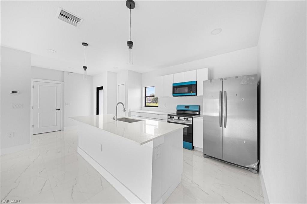 Contemporary kitchen featuring a large center island with integrated sink, white cabinetry, stainless steel appliances, and sleek pendant lighting