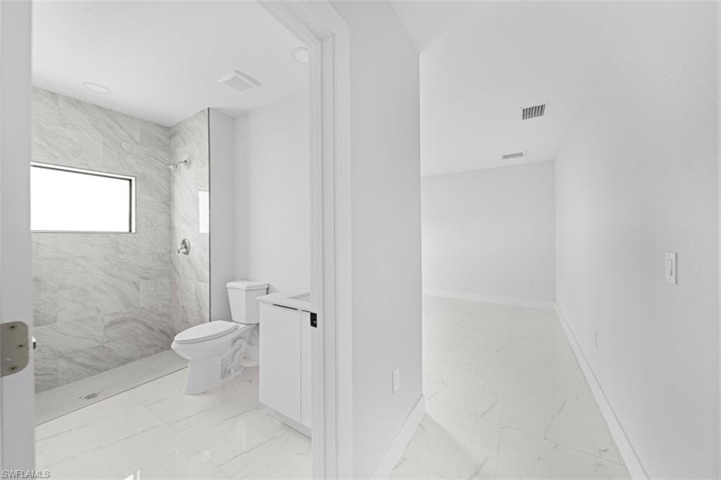 Bathroom featuring a walk-in shower with marble-look tile surround, a horizontal window, and a white vanity with a rectangular sink