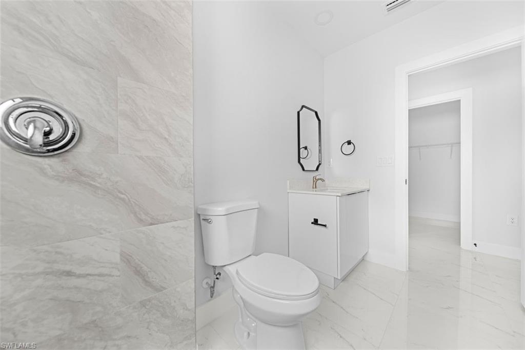 Bathroom featuring a white toilet, single vanity with white cabinetry, and a gold-finish faucet