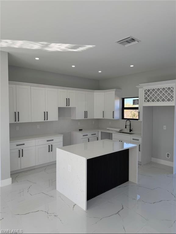Contemporary kitchen featuring white cabinetry, a waterfall-edge island with fluted detailing, quartz countertops, and large-format tile flooring