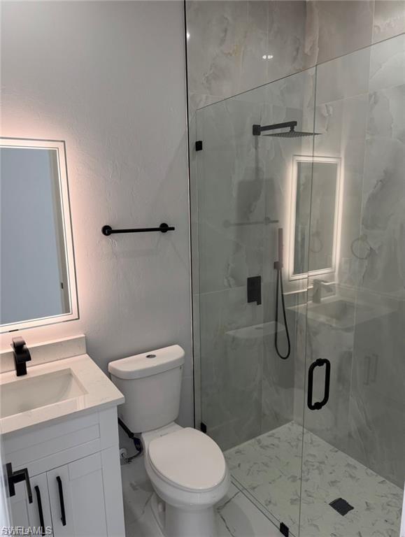 Bathroom featuring a glass-enclosed shower with rain showerhead, white vanity with integrated sink, backlit mirror, matte black fixtures, and light-toned tile flooring