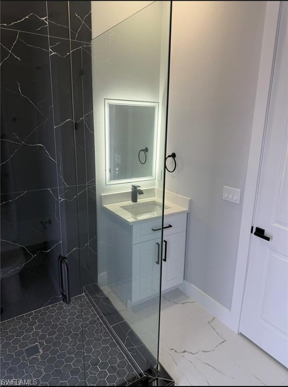Modern bathroom featuring a glass-enclosed shower with black marble-look wall tiling and hexagonal floor tiling