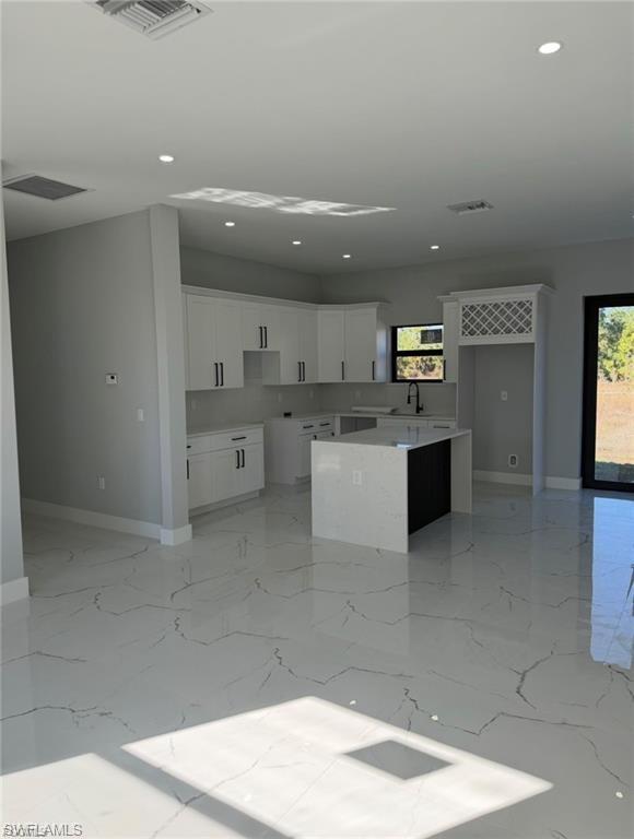 Contemporary kitchen featuring white cabinetry and a central island with a waterfall countertop