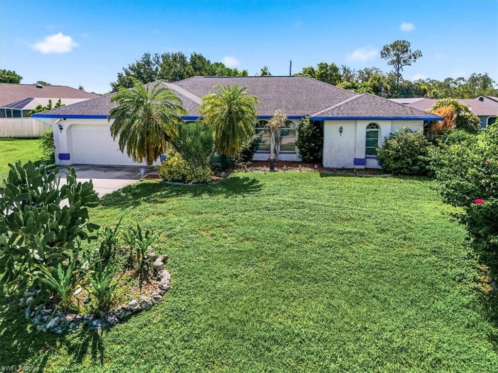 White stucco exterior with blue trim accents, featuring a two-car garage, arched window details, and mature tropical landscaping