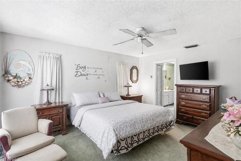 VIRTUALLY STAGED Carpeted bedroom featuring a ceiling fan, wall-mounted television, and an entryway to an adjacent bathroom with a vanity