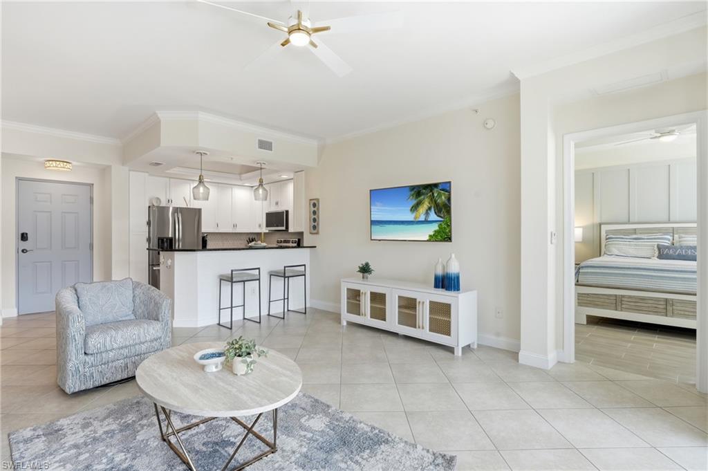 Open-concept living area featuring a kitchen with white cabinetry and a black countertop, stainless steel appliances, and a breakfast bar with pendant lighting